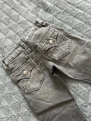 Grå jeans med detaljerade bakfickor - Snygga grå jeans med unika bakfickor som har flätade kanter och silverfärgade knappar. Jeansen är andvända fåtal gånger. Köpta på Gina tricot.
