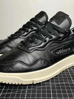 Svarta Adidas sneakers i läder - Svarta sneakers i läder med kraftig sula. Storlek 42 2/3 (EU). I mycket fint skick. Bekväma och stilrena, perfekta för vardaglig användning.