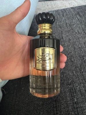 Lattafa Awraq Al Oud parfym - Aldrig använt den och pris kan diskuteras. Säljer en elegant parfymflaska från Lattafa, Awraq Al Oud. Flaskan är i glas med svart och guld detaljer, har en lyxig guldplakett och svart kork. Doften är orientalisk och flaskan har en snygg gradient från svart till bärnstensfärgat glas.