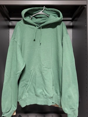 Grön oversized hoodie med huva - En grön oversized hoodie med stor känguruficka framtill och justerbar dragsko i huvan. Tillverkad i mjuk bomullsblandning och har ribbade muddar vid ärmslut och nederkant. Perfekt för en chill och avslappnad stil.