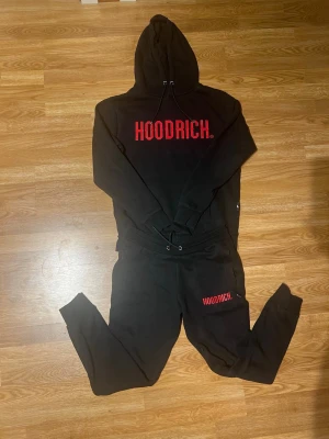 Svarta mjukisbyxor från Hoodrich - Säljer ett par svarta mjukisbyxor från Hoodrich med röd logga tryckt på vänster lår. Byxorna har resår i midjan med dragsko och är tillverkade i mjukt material som passar perfekt för en avslappnad stil.