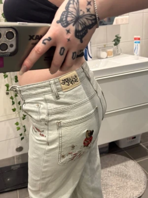 Derschutze koi fish jeans  - ✨ Derschutze Jeans – Unika & Trendiga ✨ Storlek 28 Säljer ett par snygga och ovanliga jeans från Derschutze i en ljus färg. Modellen är rak i benen med en modern passform. Byxorna har fina broderade detaljer med fiskmotiv framtill och en större brodering på bakfickan som verkligen sticker ut och ger plagget en unik look. 🐟 🪡 Hög kvalitet 👖 Baggy fit ✨ Broderade detaljer fram och bak 📍 Helt nya ! 