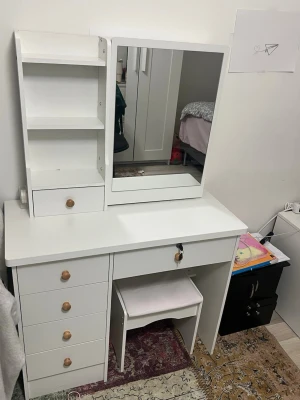 Vit sminkbord med spegel och pall - Säljer ett stilrent vitt sminkbord med stor spegel, flera lådor med träknoppar och hyllor för förvaring. Tillhörande vit pall med ljus sits ingår. Perfekt för att organisera smink, smycken och accessoarer.