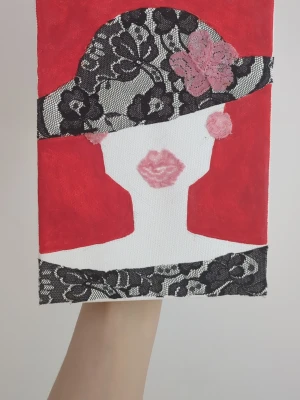 Tavla med spets och röd bakgrund - Unik tavla med motiv av en kvinna i hatt, dekorerad med svart spets och rosa blommor. Bakgrunden är intensivt röd och detaljerna är målade i vitt och rosa. Hatten och nederkanten har svart spetsmönster som ger en cool kontrast.