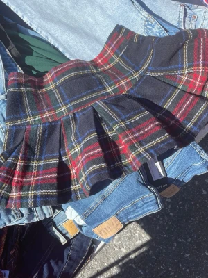 Rutig minikjol från Abercrombie & Fitch - Supersnygg rutig minikjol från Abercrombie & Fitch i mörkblått, rött, grönt och vitt. Kjolen har klassiskt skotskrutigt mönster och är plisserad för en cool och ungdomlig look. Perfekt att styla med en enkel topp eller hoodie.
