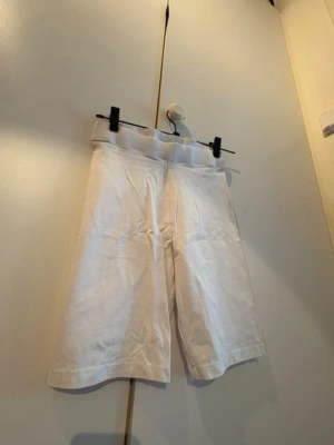 Vita cykelbyxor  - Säljer ett par vita shorts med hög midja och längre ben. De är tillverkade i mjuk bomull och har en enkel, clean design utan synliga detaljer eller fickor. Perfekta för varma dagar och en avslappnad stil.