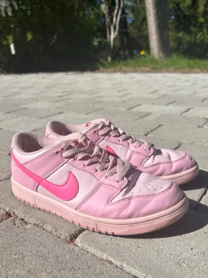 Nike Dunk Low Rosa Sneakers  - Nike Dunk Low sneakers i ljusrosa. Klassisk låg modell med perforerad tå, matchande rosa snörning och yttersula. Perfekta för dig som vill sticka ut med färg och streetstyle.