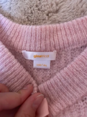 Rosa stickad kofta med rosetter Gina Tricot - Supersöt ljusrosa stickad kofta från Gina Tricot med långa ärmar och fyra dekorativa rosetter framtill. Koftan har en mjuk och fluffig känsla och ribbstickade muddar vid ärmslut och hals. Perfekt för lager-på-lager och en gullig look. Bara använd några få gånger.