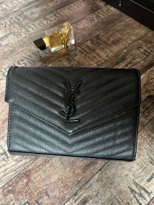 Svart handväska YSL  - YSL Saint Laurent handväska 👜 ⚠️ Saknar axelrem/kedjerem – övrigt fint skick ✅ Inga andra defekter 💡 Perfekt om du redan har en rem eller vill bära den som clutch 📦 Skickar inom 48 h på vardagar 💬 Svarar snabbt på meddelanden!