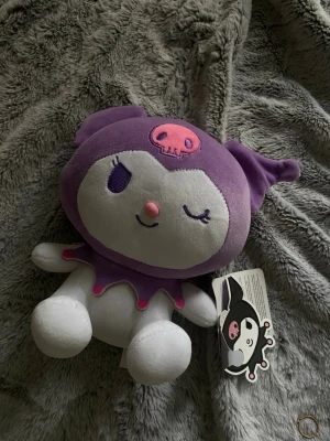Kuromi Sanrio gossedjur 25cm - Supersöt Kuromi gosedjur från Play by Play, officiellt licensierad av Sanrio. Mjuk plysch i lila och vitt med rosa detaljer och en liten dödskalle på huvan. Perfekt för dig som gillar kawaii och samlar på Sanrio-figurer. Finns lappen kvar, gjord av sanrio och köpt på kryssning. 25 cm på höjden !