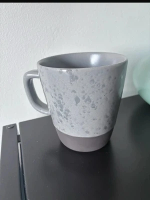 Grå mugg från RAW Crafted Concept - Säljer en snygg grå mugg från RAW Crafted Concept. Muggen har en matt finish med prickigt mönster och en mörkare grå botten. Perfekt för kaffe eller te och har ett rejält handtag. Tillverkad i keramik.
