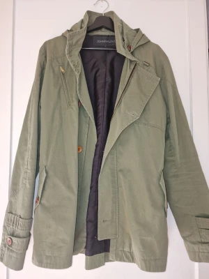 Olivgrön trenchcoat från JohnnyLove - Olivgrön kappa med avtagbar huva från JohnnyLove. Avslappnad passform och snygga detaljer på ärmar och fickor. Perfekt för dig som gillar stilren och funktionell design. Inköp i Norge för ca 4500 kr. Använd ca 6-7 gånger.