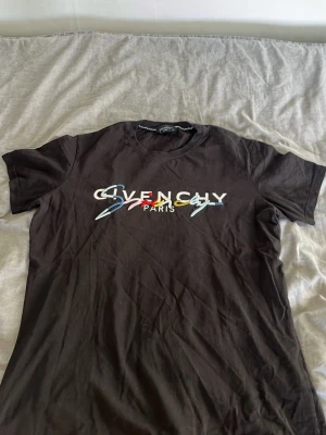 Svart Givenchy t-shirt med färgglatt tryck - Snygg svart t-shirt från Givenchy med ett färgglatt och grafiskt tryck på bröstet där det står 'Givenchy Paris'. Klassisk rund halsringning och korta ärmar. Tillverkad i mjuk bomull som känns skön mot huden.