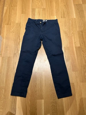 Mörkblå chinos med rak passform - Snygga mörkblå chinos med klassisk rak passform och knappgylf. Byxorna har framfickor och bakfickor, perfekta för en stilren look. Tillverkade i ett mjukt och bekvämt bomullsmaterial. Stål 31 i midja