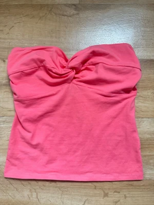 Korall bandeau tubtopp med twist - Snygg korallrosa bandeau tubtopp med twistad detalj framtill. Toppen är ärmlös och har en figurnära passform, perfekt för varma dagar. Tillverkad i mjukt bomullsmaterial som känns skönt mot huden.