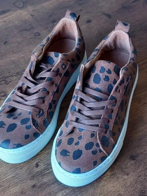 Bruna sneakers från Pieces med leopardmönster storlek 36 - Snygga bruna sneakers från Pieces med svart leopardmönster och vita sulor. Skorna har klassisk låg modell med snörning och är tillverkade i mocka material. Perfekta för dig som vill sticka ut med ett djurmönstrat statement.