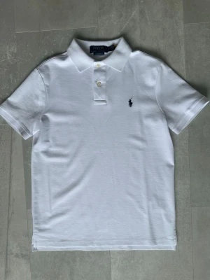 pikétröja från Polo Ralph Lauren - Klassisk vit pikétröja från Polo Ralph Lauren, endast använd någon enstaka gång. Tillverkad i mjuk bomull som känns skön mot huden. En stilren och tidlös piké som passar perfekt till både vardag och finare tillfällen. Den är även helt ny och har inte används. Men prislapparna finns inte kvar.