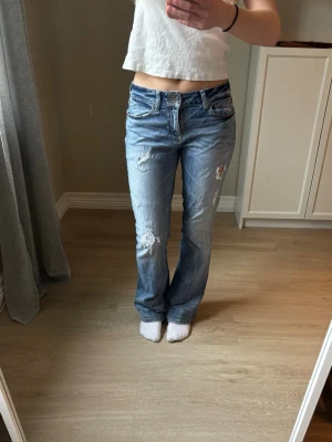 Blå bootcut jeans med slitningar - Säljer ett par blå bootcut jeans med slitna detaljer. Jeansen har klassisk femficksdesign, normalhög midja och är tillverkade i denim. Perfekta för en avslappnad och trendig look.            Midjemått: 38 cm                                                         Innerbensmått: 78 cm 