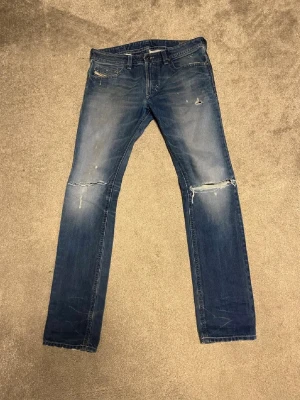 Diesel jeans  - Säljer ett par blå jeans med normal och rak passform med fades och slitningar samt hål vid båda knäna. Jeansen har klassisk femficksdesign och är tillverkade i denim. Perfekta för en avslappnad och trendig streetstil.