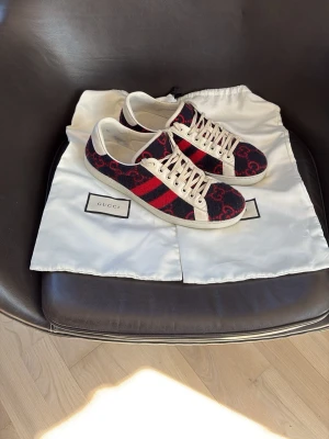 Gucci skor - Gucci sneakers i tyg med klassiskt GG-mönster i rött och blått, vita detaljer och snörning. Skorna har de ikoniska röda och blå ränderna på sidan och vit sula. Perfekta för dig som vill sticka ut med lyxig streetstyle.