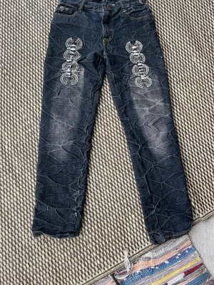 Mörkblå tribal-mönstrade jeans - Unika mörkblå jeans med tribal-inspirerade tryck på framsidan av benen och broderade bakfickor med texten 'TRIBAL CHILTORE'. Raka ben och klassisk femficksmodell. Snygga detaljer och slitningar framtill för en cool look.