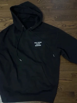 Drole de monsieur  - Svart hoodie från Not From Paris Madame med vit broderad text på bröstet. Klassisk modell med huva och dragsko samt känguruficka framtill. Perfekt för en chill och stilren look.