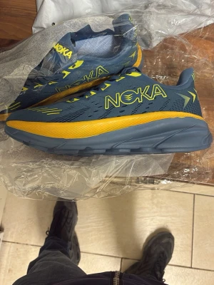 Blå och gula sneakers från  - Snygga sneakers i blått med gula detaljer och logga på sidan. Ovandelen är i mesh för bra andningsförmåga och sulan är rejäl och mönstrad för extra grepp. Perfekta för dig som vill sticka ut med färg och stil.