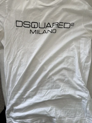 Vit DSQUARED2 t-shirt med tryck - Vit t-shirt från DSQUARED2 med svart texttryck 'DSQUARED2 MILANO' på bröstet. Klassisk rund halsringning och korta ärmar. Perfekt för en stilren och trendig look. Pris kan diskuteras.