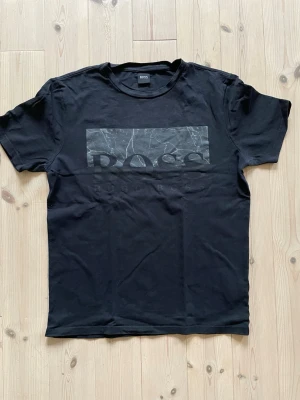 Svart Hugo Boss t-shirt med tryck - Snygg svart t-shirt från Hugo Boss med stort marmorerat tryck och logga på bröstet. Klassisk rund hals och korta ärmar. Tillverkad i mjuk bomull. 