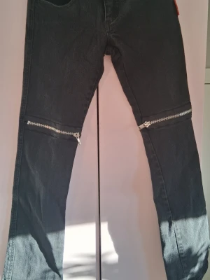 Svarta jeans med dragkedjor från Tripp NYC - Säljer ett par svarta jeans från Tripp NYC med feta silverfärgade dragkedjor över knäna. Jeansen har en rak passform och klassisk femficksdesign. Perfekta för dig som gillar alternativ stil och vill sticka ut lite extra. 