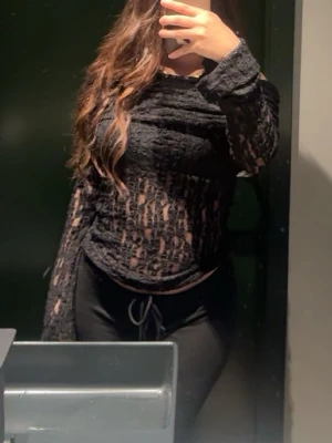 Svart offshoulder mesh topp - Trendig svart offshoulder topp i mesh med transparent spetsdetaljer. Långärmad och figurnära passform som ger en edgy look. Perfekt att styla med höga byxor eller kjol för en cool outfit. Har använt den 1 gång.