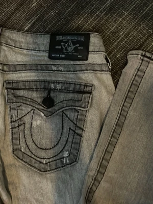Grå True Religion jeans  - Måste tyvärr sälja dem här jättefina gråa jeansen från True Religion pågrund av att de är lite stora. Jeansen är lågmidjade utan några synliga defekter (använd någon enstaka gång) storlek 27.