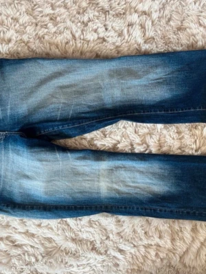 Blå jeans med dekorerade bakfickor - Säljer ett par blå jeans med slitningar och snyggt tvättad look. Bakfickorna är dekorerade med pärlor, paljetter och broderade detaljer som ger en unik och trendig stil. Perfekta för dig som vill sticka ut lite extra i vardagen. Storlek 38