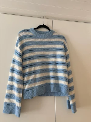 Blåvit stickad tröja med hålmönster - Supersöt stickad tröja i ljusblått och vitt med breda ränder och hålmönster. Tröjan har ribbade muddar vid ärmslut och nederkant samt en rund halsringning. Perfekt för dig som gillar en avslappnad men trendig stil. Stl XS men passar absolut S.