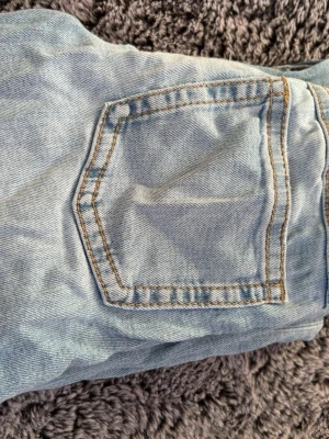 Ljusblå bootcut jeans - Säljer ett par ljusblå bootcut jeans med klassiska fem fickor och kontrastsömmar. Jeansen har en utsvängd passform nedtill och är tillverkade i denim. Perfekta för en avslappnad och trendig look. Dom är lite skrynkliga men det går arr lösa enkelt!