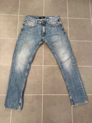 Blå raka jeans från Replay - Säljer ett par klassiska blå jeans från Replay med raka ben och snyggt slitna detaljer på låren. Jeansen har fem fickor, normal midja och är gjorda i ett mjukt denimtyg. Perfekta för en avslappnad och trendig look.