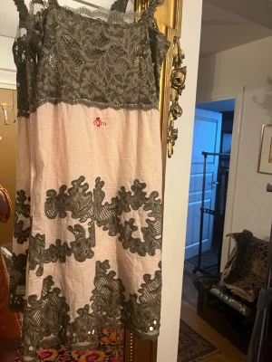 Rosa spetsklänning från Odd Molly - Supersöt kort klänning från Odd Molly i ljusrosa med grå spetsdetaljer och paljetter. Klänningen har tunna axelband, vackert spetsmönster upptill och nertill samt dekorativa broderier. Perfekt för dig som gillar romantisk och unik stil.