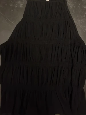 Svart linne med volanger från H&M - Säljer ett svart linne med volangdetaljer och ett snyggt, rynkat tyg. Klänningen har en luftig passform och är perfekt för dig som gillar en enkel men elegant look. Tillverkad i ett mjukt material som känns skönt mot huden.