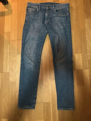Blå raka jeans från J.Lindeberg - Säljer ett par klassiska blå jeans med rak passform och fem fickor från J.Lindeberg. Jeansen har en lätt tvättad look och normal midja. Materialet är denim i bomull och de har bälteshällor samt knappgylf. Perfekta till en avslappnad stil.