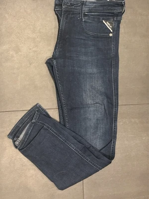 Mörkblå Replay Anbass jeans - Säljer ett par mörkblå jeans från Replay, modell Anbass. Jeansen har en smal passform och med Replay-logga på fickan. Materialet är stretchigt denim som ger en bekväm känsla. Storlek Waist 29 och Lenght 30.