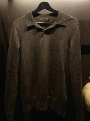 Olivgrön/brun stickad tröja från Morris - Säljer en olivgrön/brun stickad tröja från Morris i 100% merinoull. Tröjan har klassisk krage och långa ärmar, perfekt för dig som gillar stilrena och tidlösa plagg. Passar lika bra till jeans som till chinos.