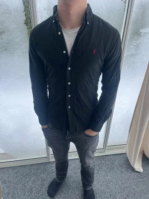 Svart skjorta från Ralph Lauren - Riktigt snygg skjorta från Ralph Lauren. Riktigt bra passform. Strl S. Personen på bilden är 184 cm lång. Skicka gärna prisförslag. Fraktas dagen efter köp.