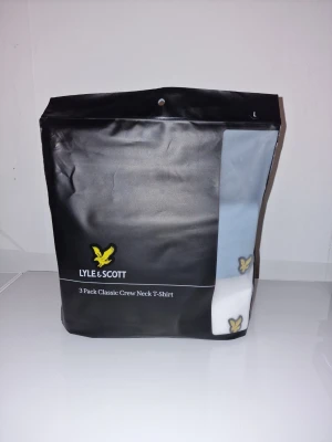 T-shirt från Lyle & Scott - Klassisk t-shirt från Lyle & Scott med den ikoniska gula loggan broderad nere vid fållen. Tillverkad i mjuk bomull och har en enkel, clean design som passar till allt. Perfekt basplagg för din garderob.