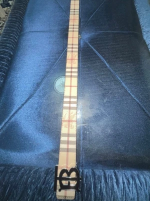 Vändbart Burberry bälte med BB-spänne - Säljer ett vändbart Burberry bälte med klassiskt rutigt mönster på ena sidan i beige, rött och svart samt svart diskret rutmönster på andra sidan. Stort BB-spänne i metall framtill. Perfekt accessoar för att lyfta din outfit.