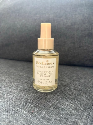 Beelicious Vanilla Cream Body & Hair Perfume - Beelicious Vanilla Cream är en kropp- och hårparfym med honungsextrakt. Kommer i en genomskinlig glasflaska med beige spraykork och etikett. Doften har inslag av vanilj och krämiga toner. 