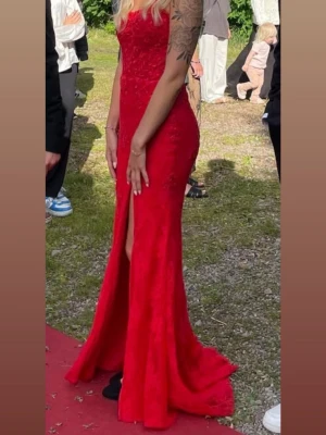 Röd balklänning med slits - (Intressekoll) Elegant röd balklänning med figurnära passform och v-ringad urringning. Klänningen har fina spetsdetaljer och en hög slits framtill som ger en snygg siluett. klänningen har även små diamant detaljer i spetsen!  Perfekt för bal eller festliga tillfällen. Klänningen är sydd för min kroppsform, jag väger 59kg och är 170cm lång. Passar Xs/S! Endast använd 1 gång! Köpte klänningen nypris 7k. Klänningen är ifrån Ruths i västerås
