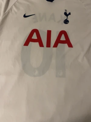Tottenham Hotspur Kane matchtröja - Vit Tottenham Hotspur matchtröja från Nike med tryck 'KANE' och nummer 10 på ryggen. Framsidan har klubbens logga, Nike-logga och sponsortryck i rött. Tillverkad i lätt och ventilerande material, perfekt för fotbollsträning eller match.