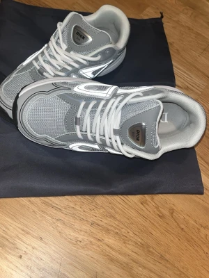 Grå fina skor - Snygga sneakers i grått med vita och silverdetaljer. Skorna har en chunky sula, meshpaneler och reflekterande logga på sidan. Klassisk snörning och bekväm passform, perfekt för dig som gillar exklusiva och trendiga sneakers.