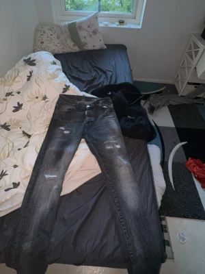 Svarta Dsquared2 slitna jeans - Säljer ett par svarta jeans från Dsquared2 med slitningar och tvättade detaljer för en cool, använd look. Jeansen har rak passform och klassisk femficksdesign. Perfekta för dig som gillar streetwear och vill sticka ut lite extra.