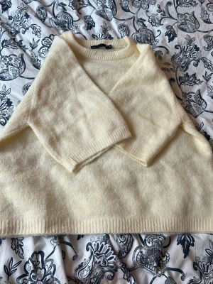 Ljusgul stickad T-shirt ullmix - Mysig ljusgul stickad T-shirt med rund hals och långa ärmar. Tröjan har en avslappnad passform och ribbade muddar vid ärmslut och nederkant. Perfekt för lager på lager och ger en soft vibe till din outfit.